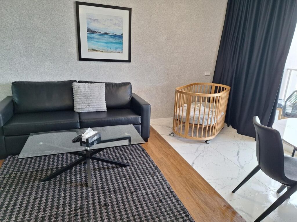 Living space with black leather couch and baby cot at Honeysuckle Superior One Bedroom Apartment