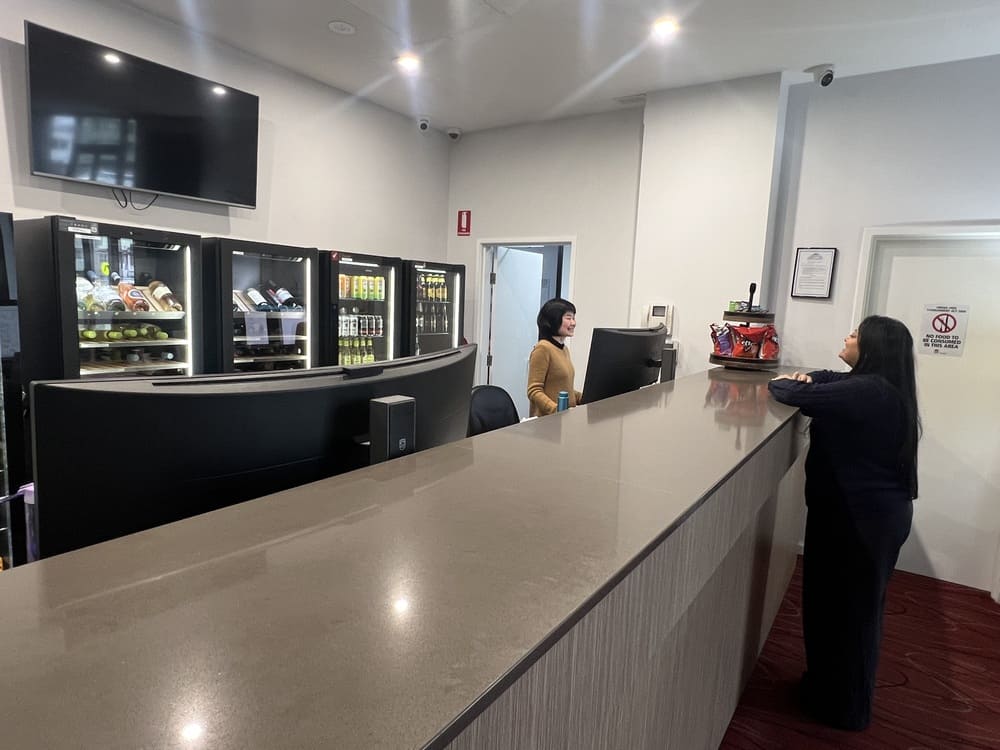 Reception area at Honeysuckle Executive Apartments with staff, snack display, and fridges stocked with drinks