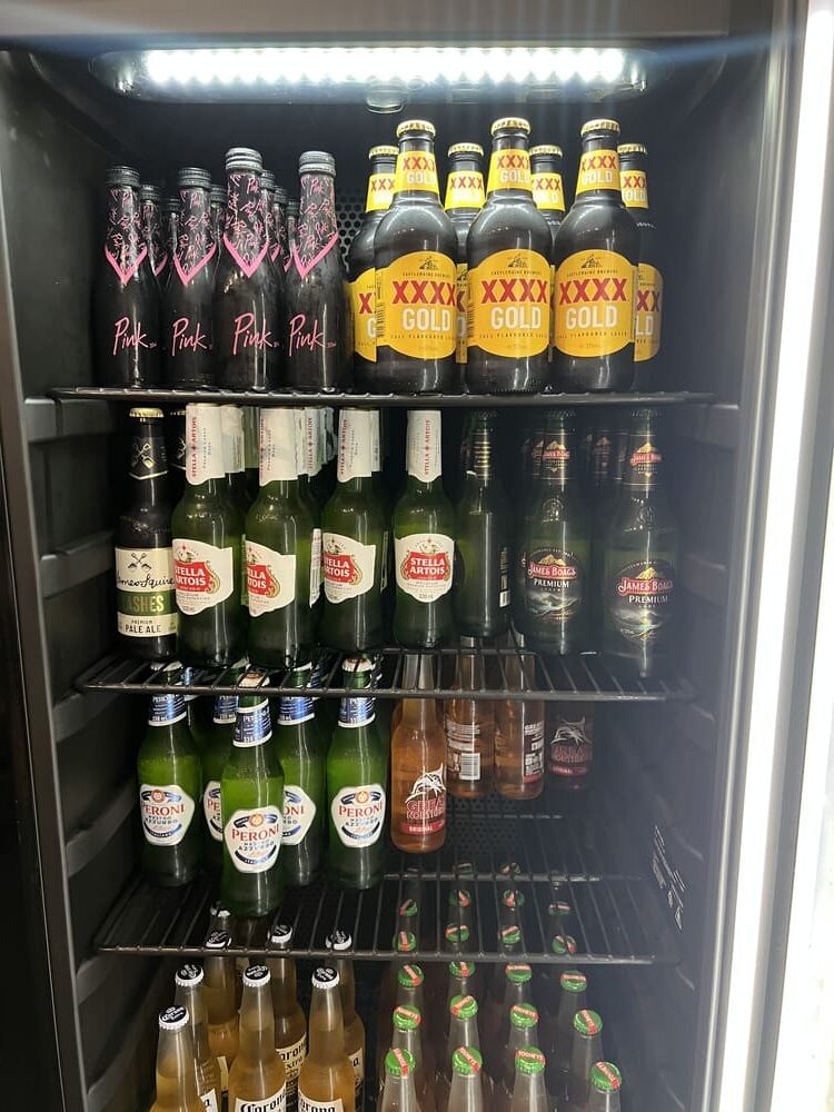Fully stocked mini bar fridge at Honeysuckle Executive Apartments featuring beer, cider and premix drinks